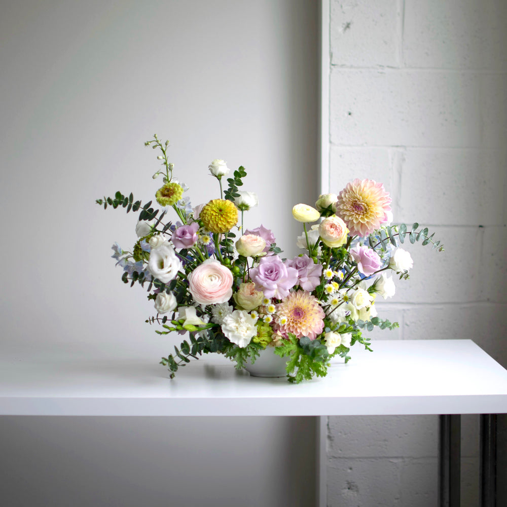 Light purple and cream flower bouquet with muted yellow accents on a white table.