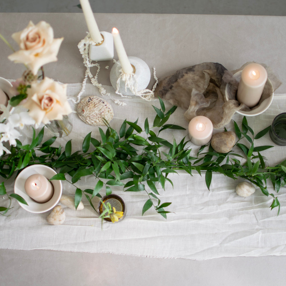A simple fresh greenery garland runs along a white tablecloth, which is littered with candles.
