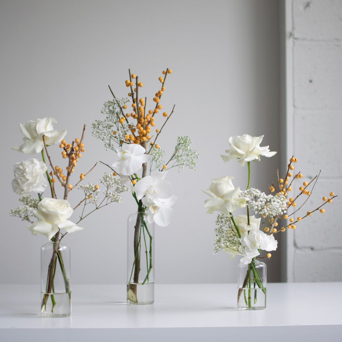 Winter themed trio of glass bud vases with white roses.