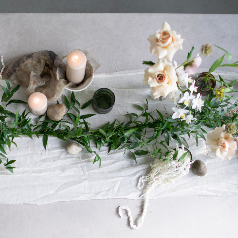 A simple table runner made of fresh greenery sits among neutral accents and minimal flowers.
