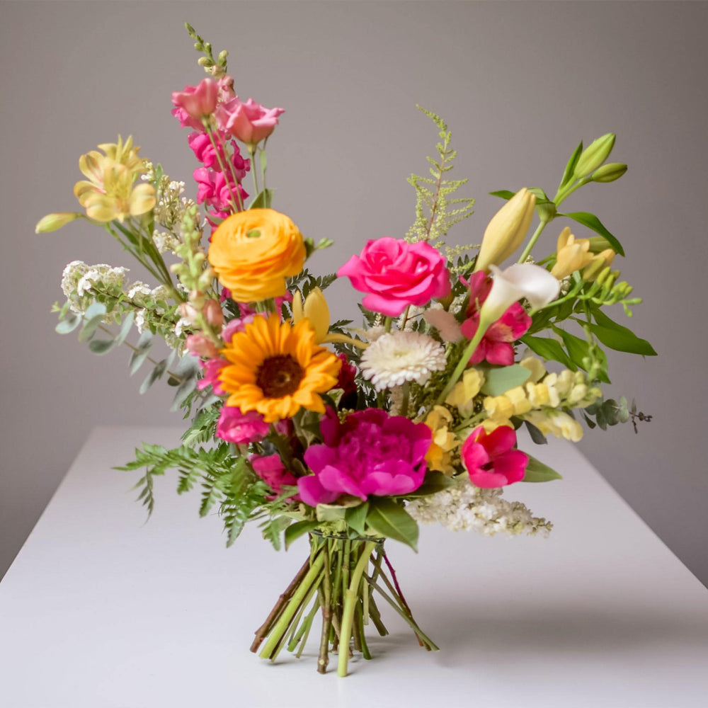 Yellow sunflowers and rich pink roses  are visible in this bright hand-tied bouquet.