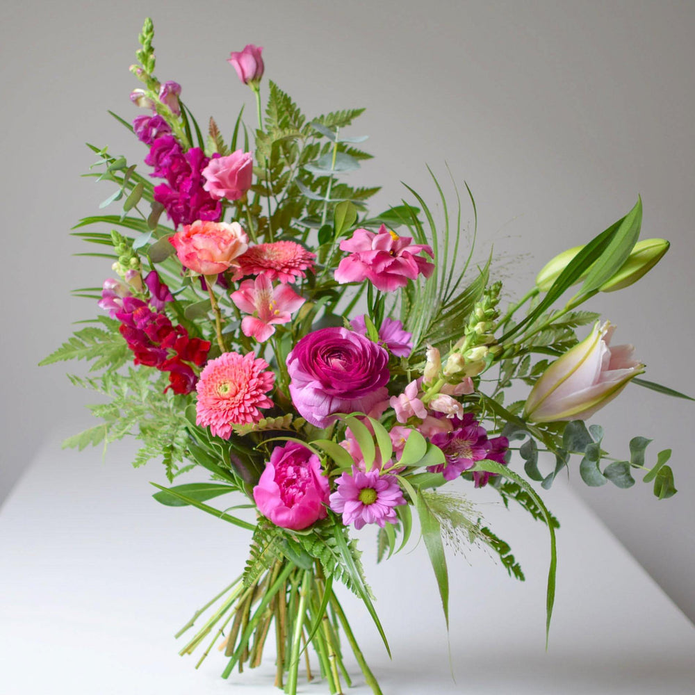 Bold pinks and vibrant fresh greens make up a hand-tied flower bouquet.