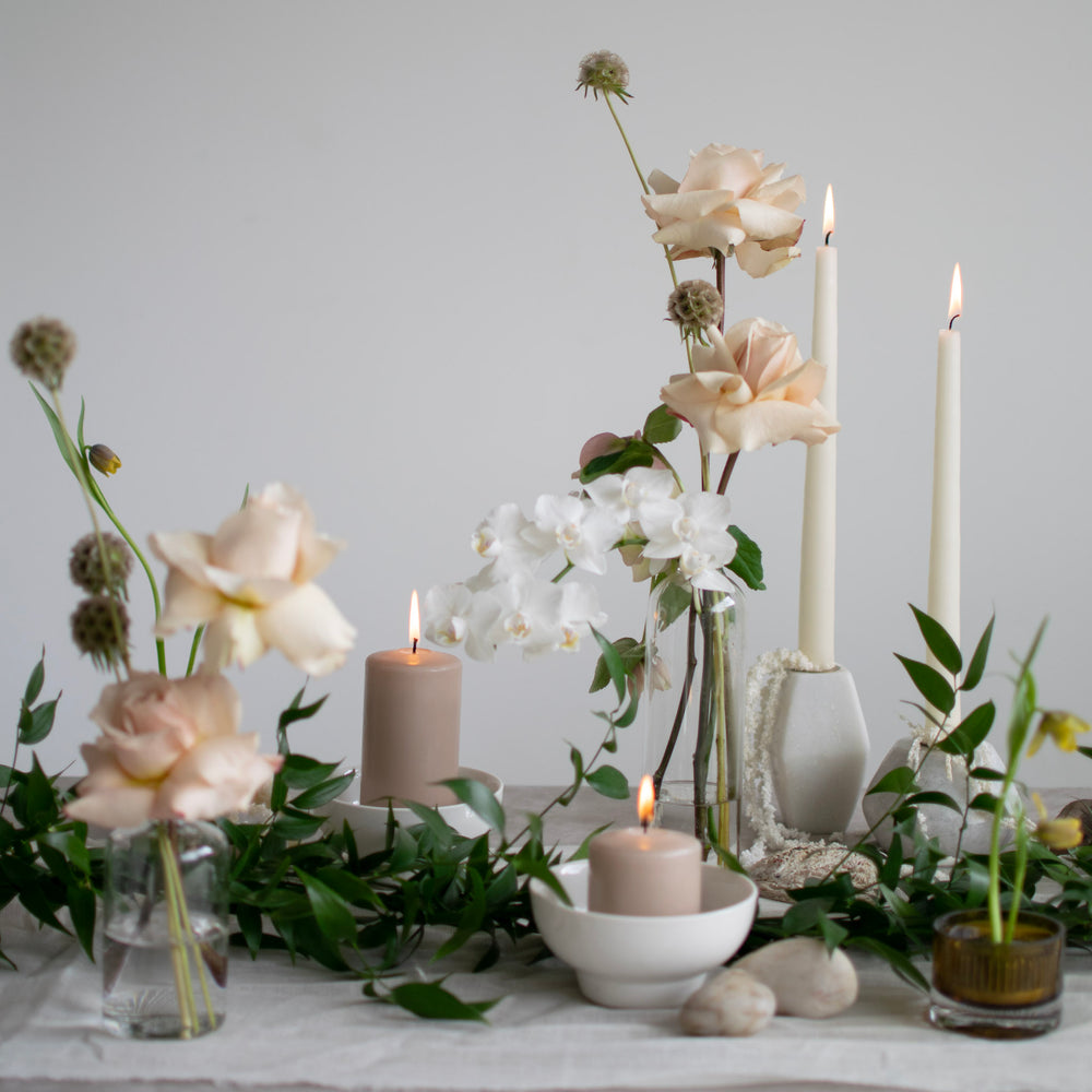 Light pink flexed roses, white orchids, and lots of greenery is visible on this candle lit tablescape.
