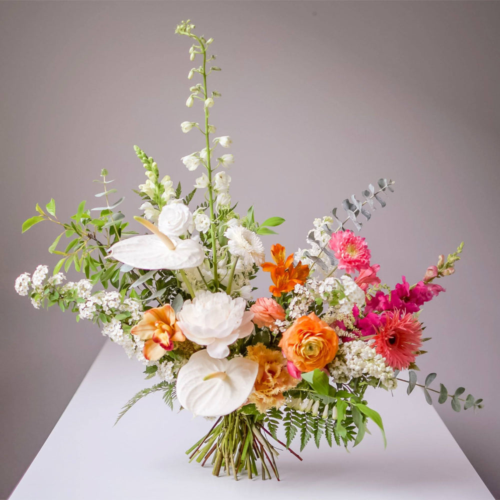 Bright white, pink, and orange floral bouquet on a white table.