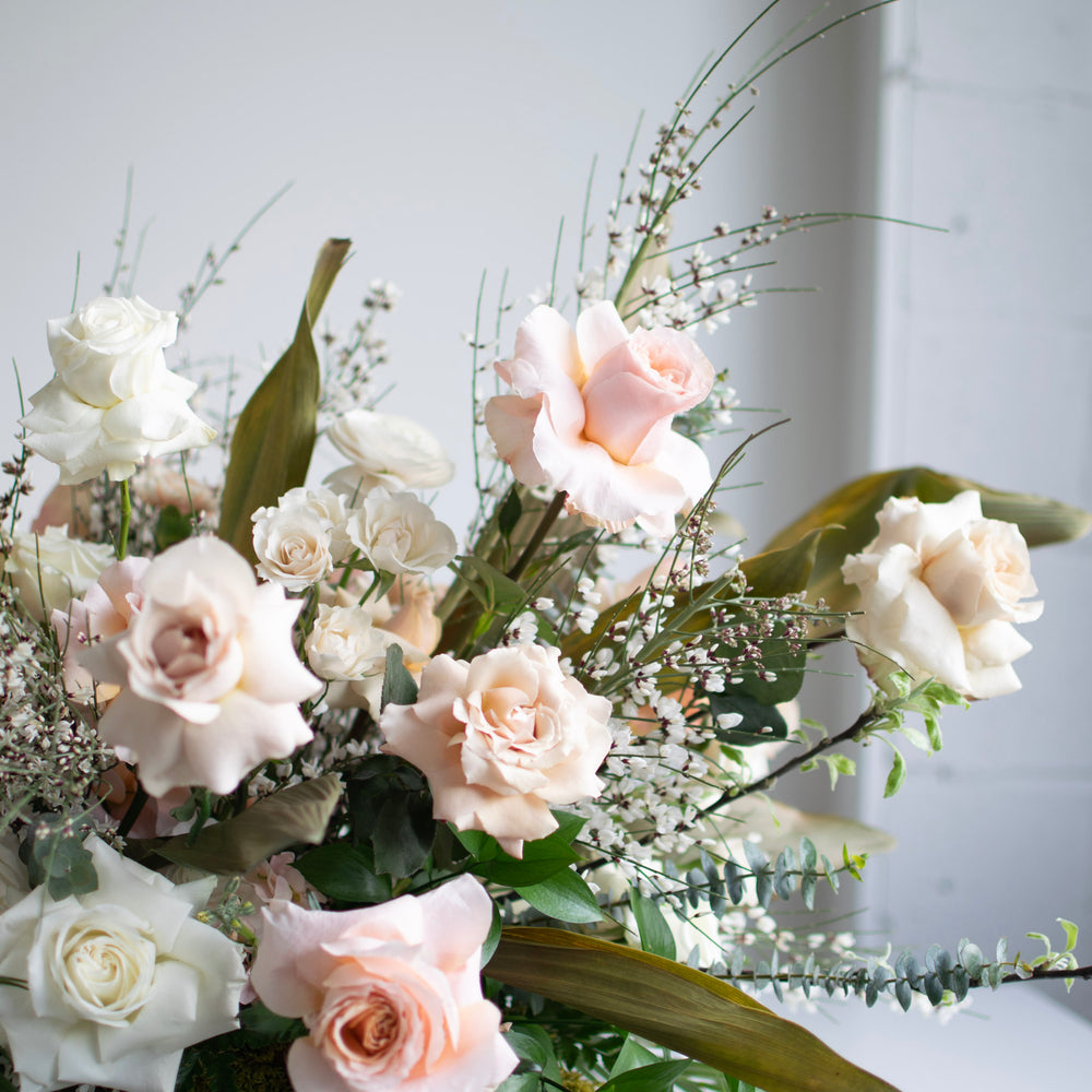 Light pink and white roses reach out of a large floral arrangement.