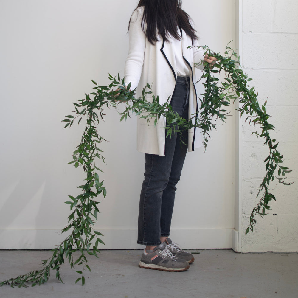A woman with a long white coat holds a simple, thin greenery garland.