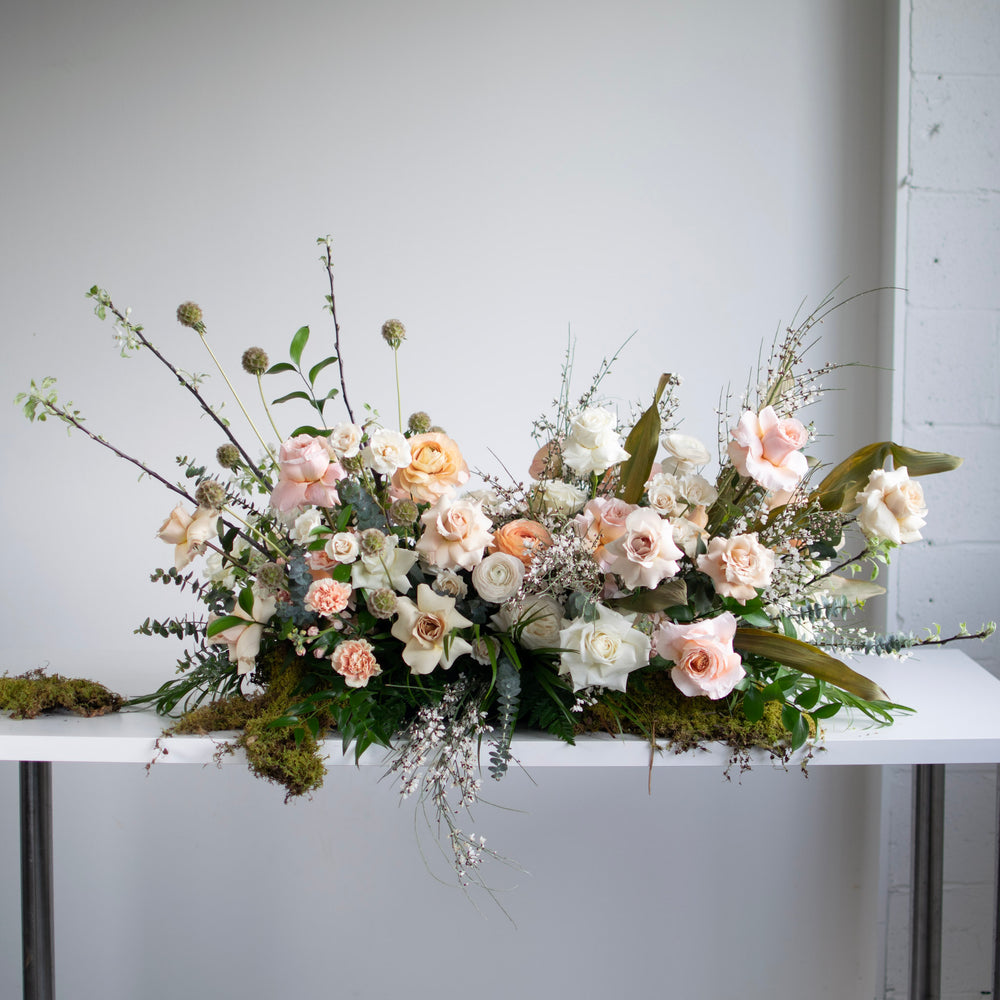 A garden-style casket spray using moss and a soft pink palette.