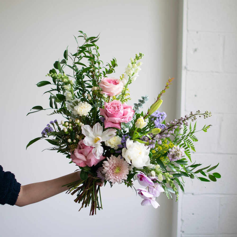 A large hand-tied bouquet with roses, lilies, and orchids in a soft palette.