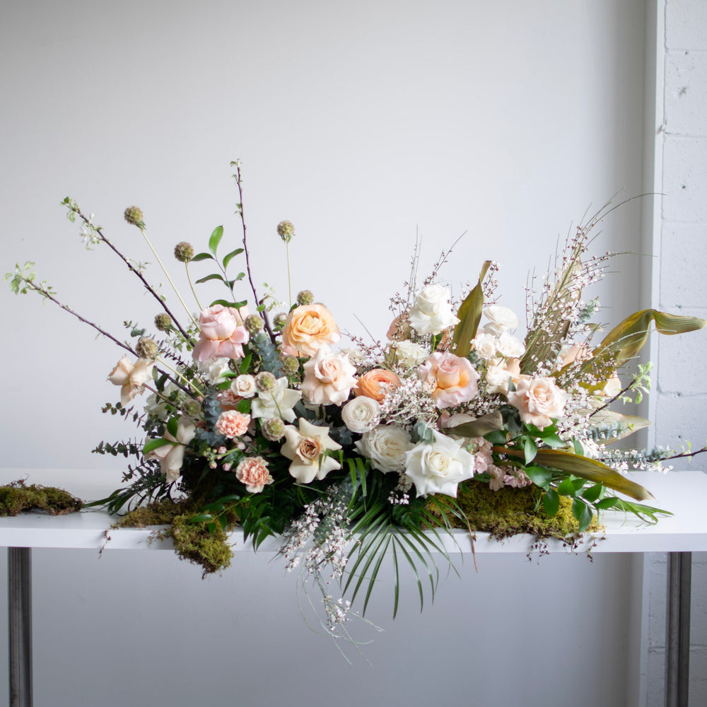 A large, whimsical casket spray with tones of white, cream, peach, and light pink.