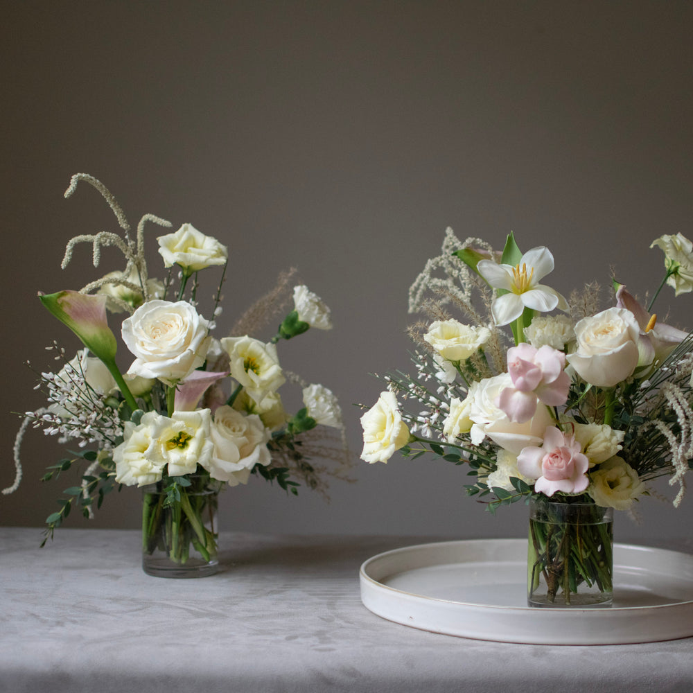 Two small wedding centrepieces with white and light pink flowers, including calla lilies.