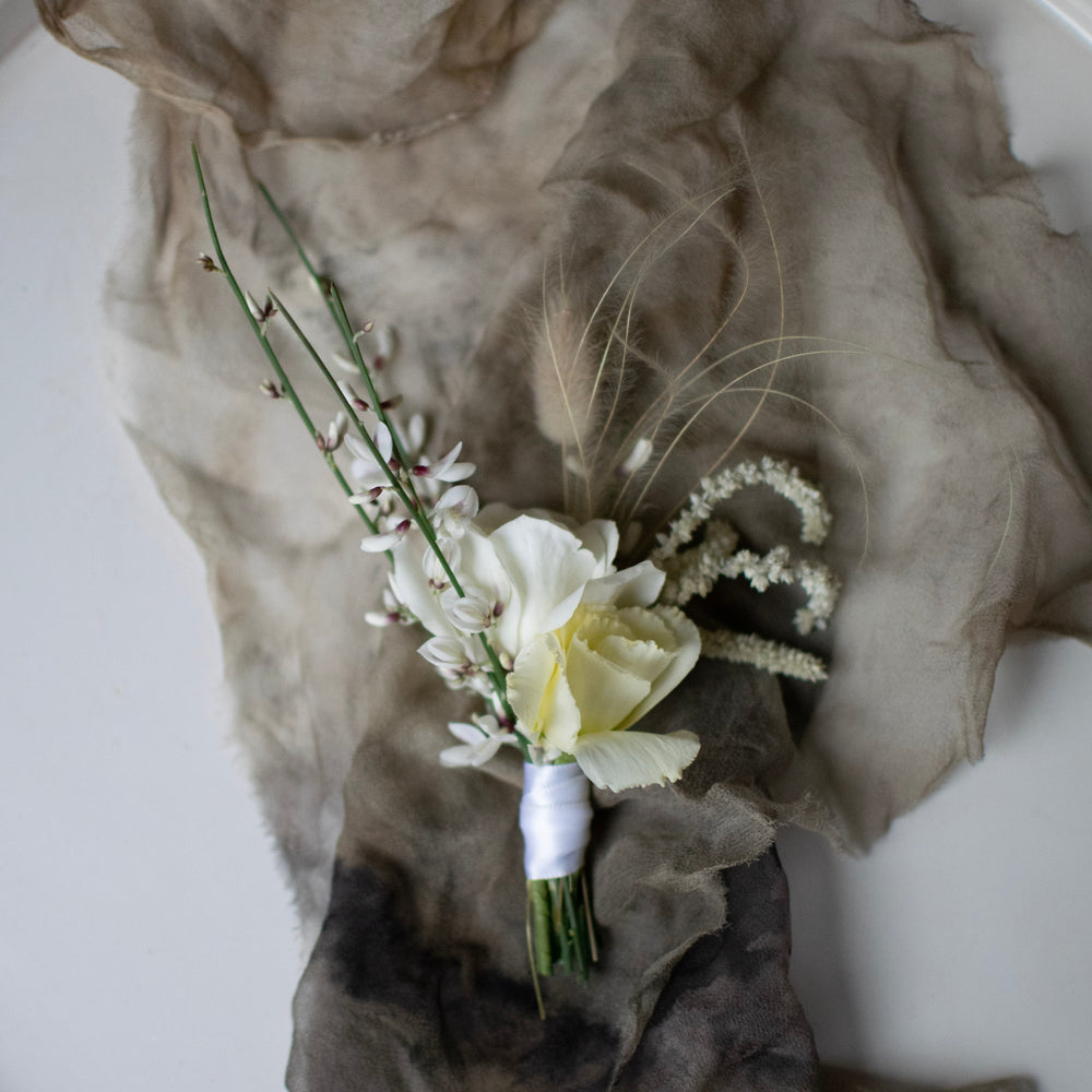 An all-white boutonniere sits against a smokey grey cloth.