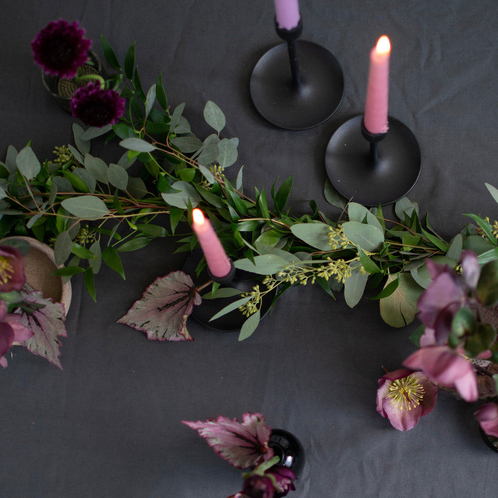 A greenery garland is wrapped around tapered candle holders and glossy glass vases.