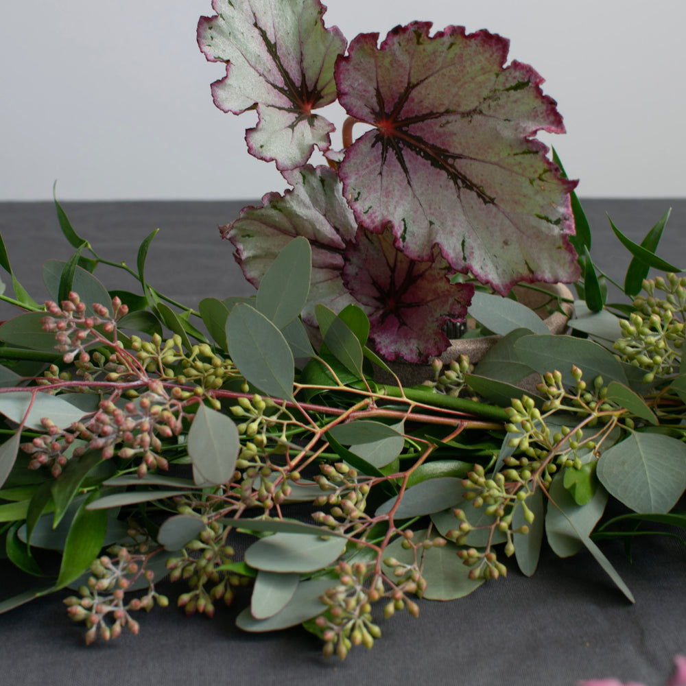 A fresh greenery table garland with purple accents on a navy tablecloth.