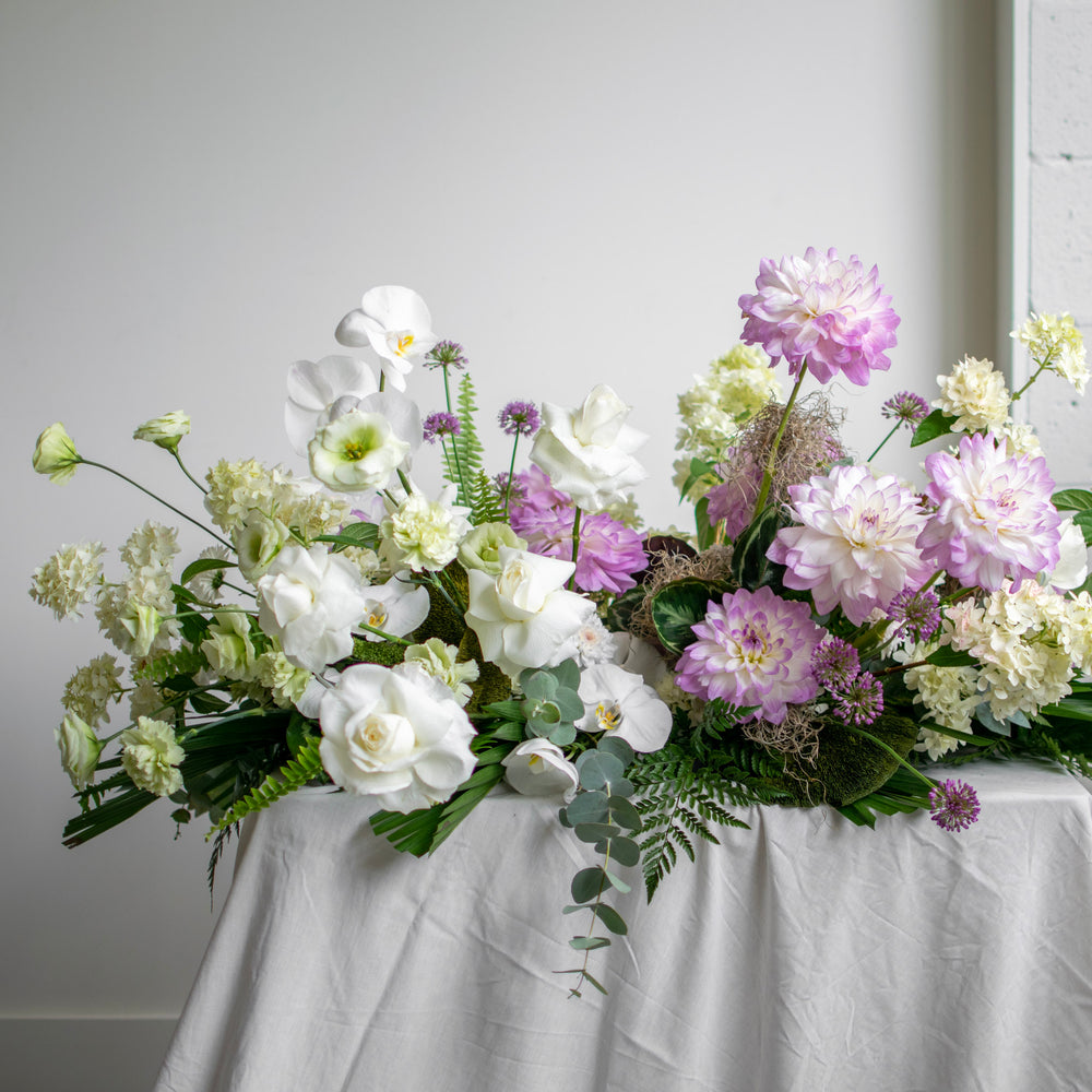 A large, two toned casket spray with white and purple ombre flowers.