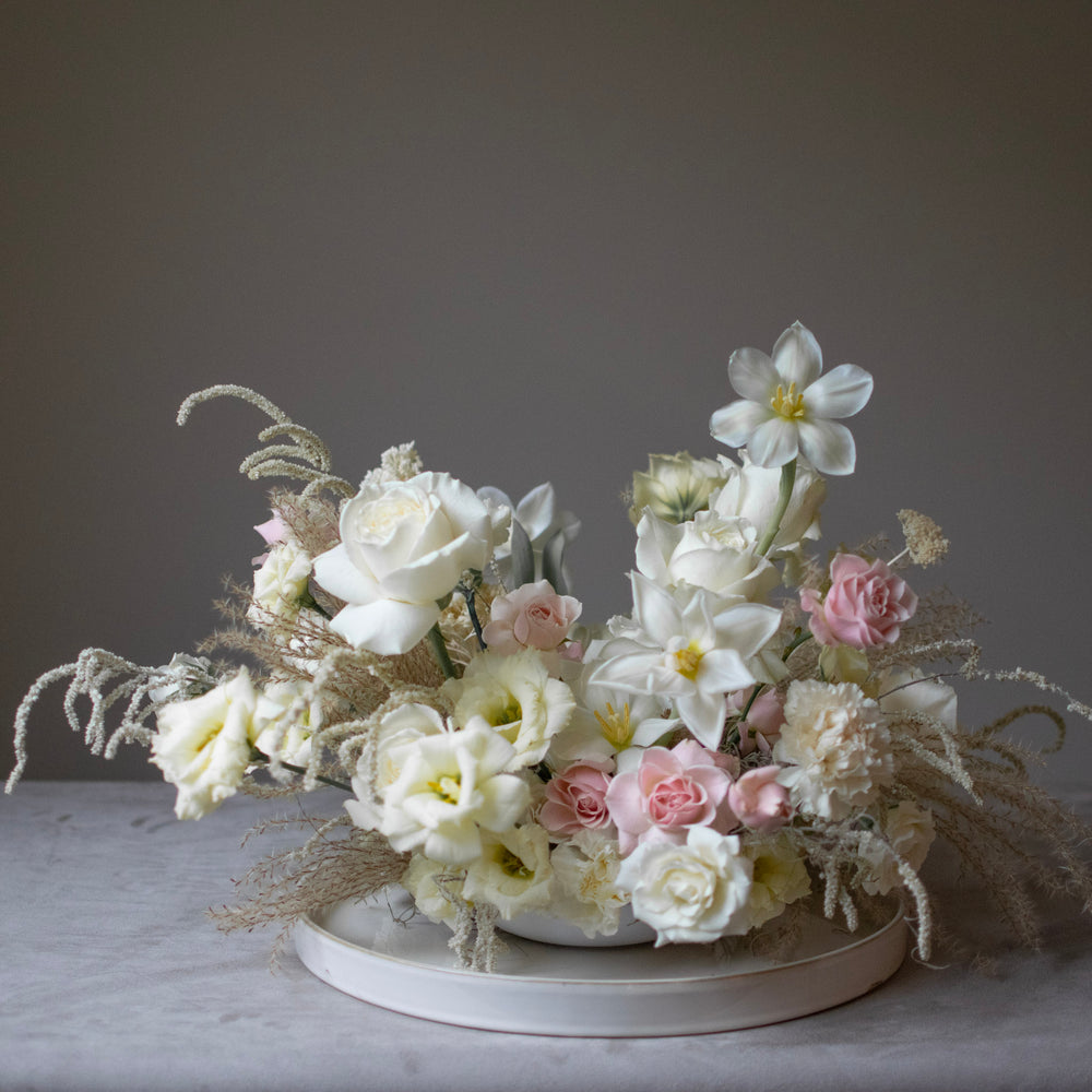 An all-white, elegant wedding centrepiece with flexed tulips and pink rose accents.