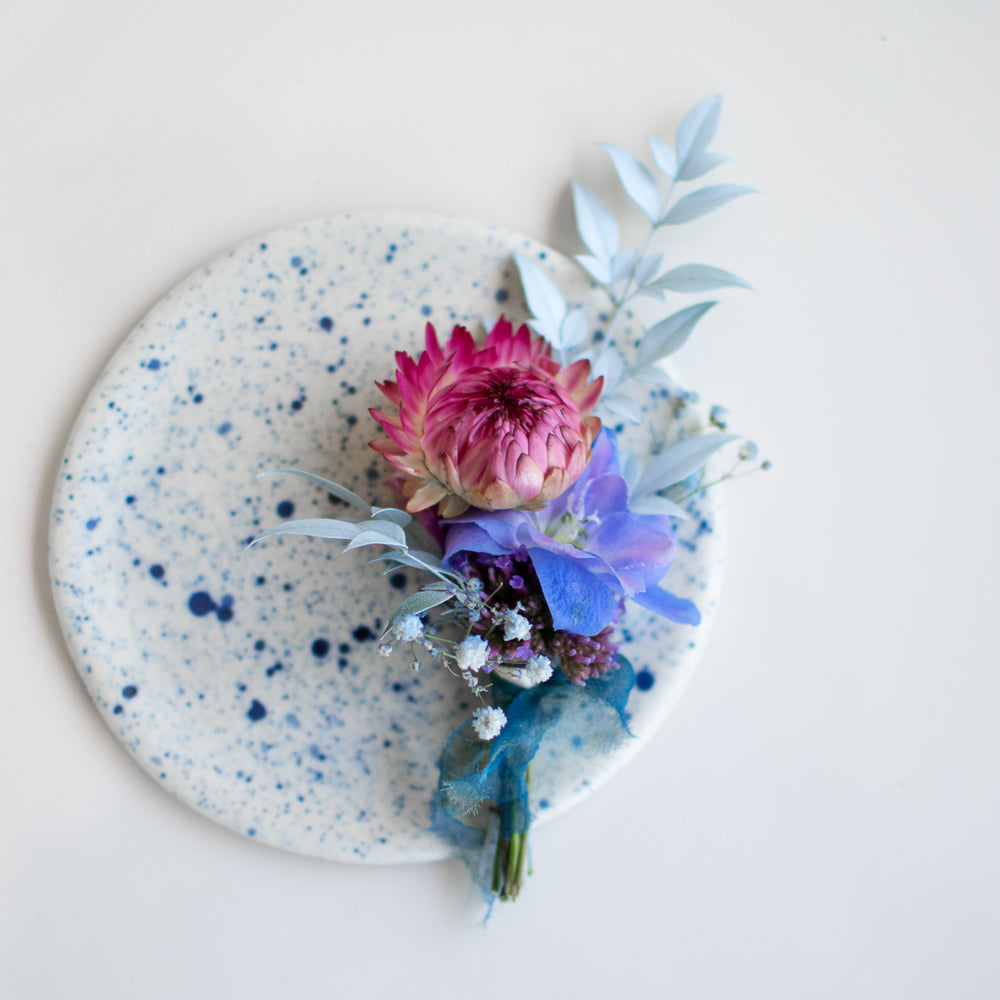A blue and pink boutonniere sits against a marble coaster, also speckled with blue.