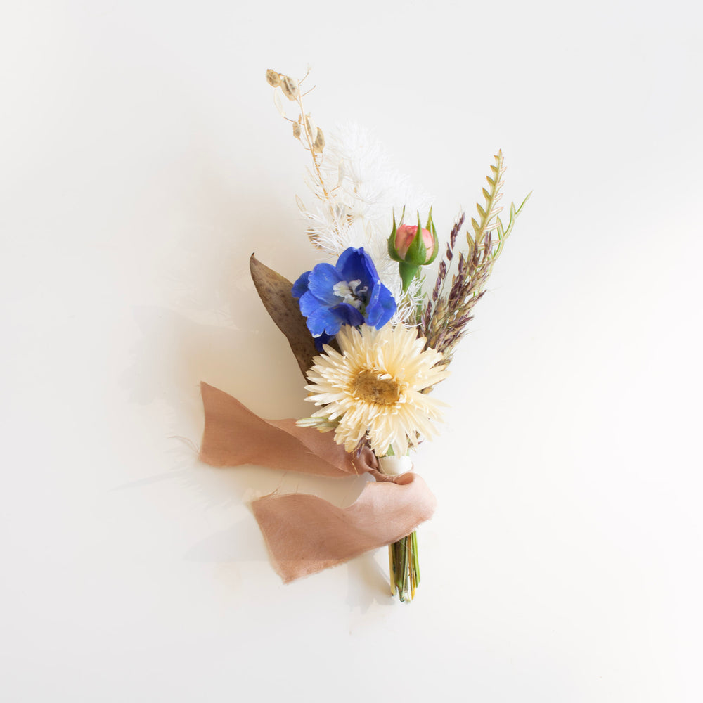 A dried boutonniere with a muted palette. A dusty pink ribbon is tied around the stems.