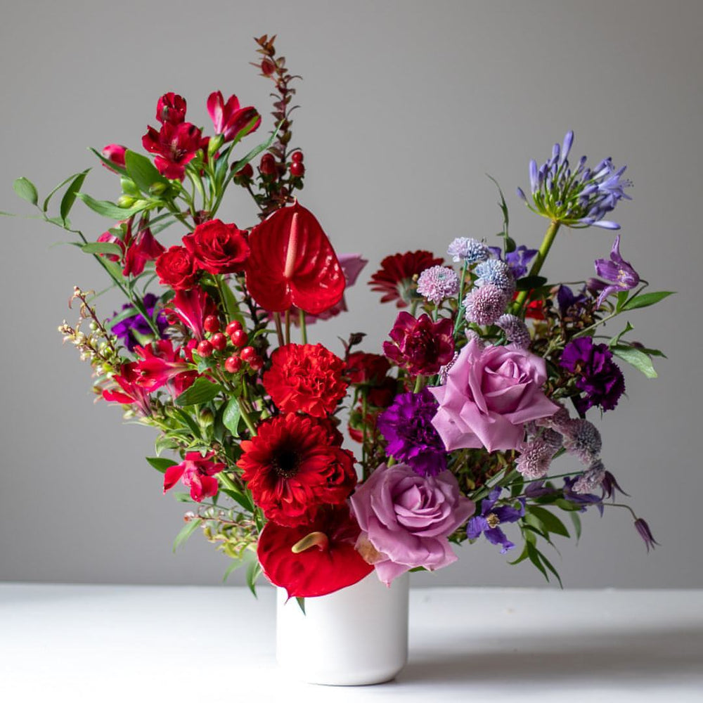 Romantic flower arrangement in deep red and luxurious purples with lots of roses.