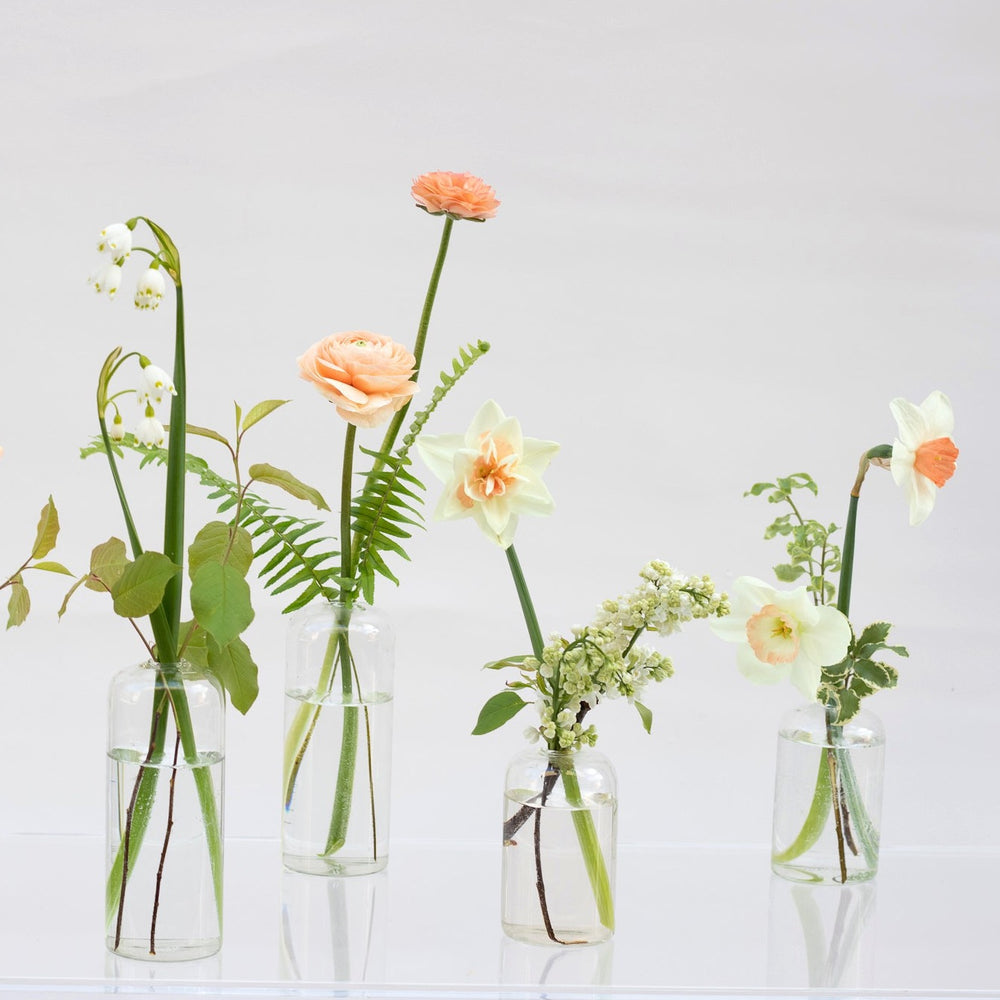 Simple greenery and delicate peach flowers in glass vases.