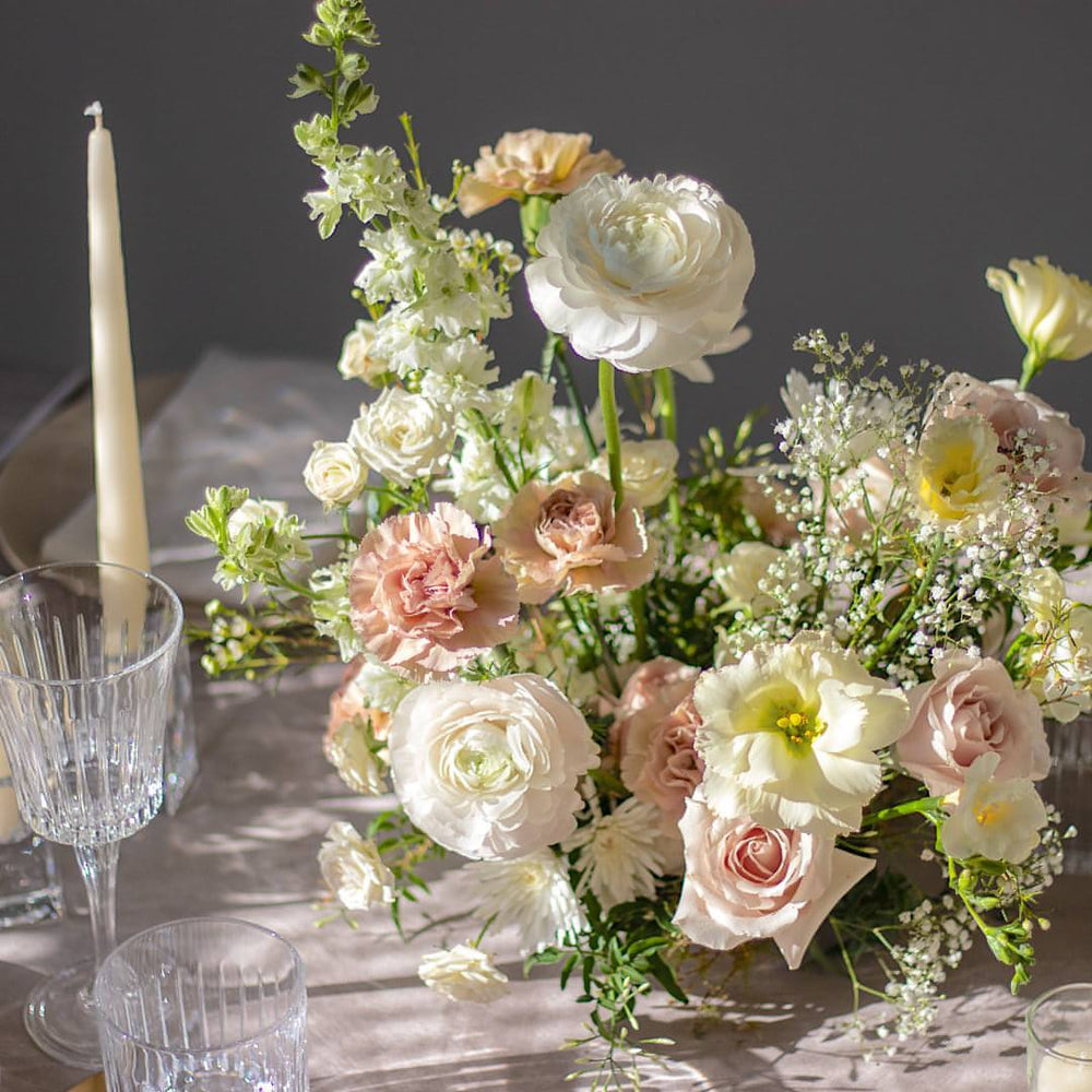 Light pink carnations, ranunculus, and baby's breath are visible in a floral centrepiece amidst tableware.