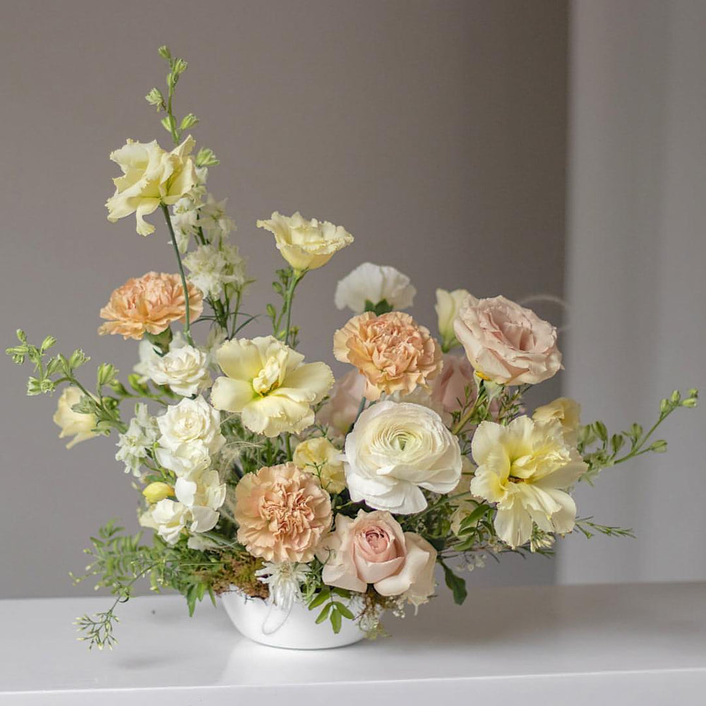 A floral arrangement with whites, creams, and blush carnations in a bowl.