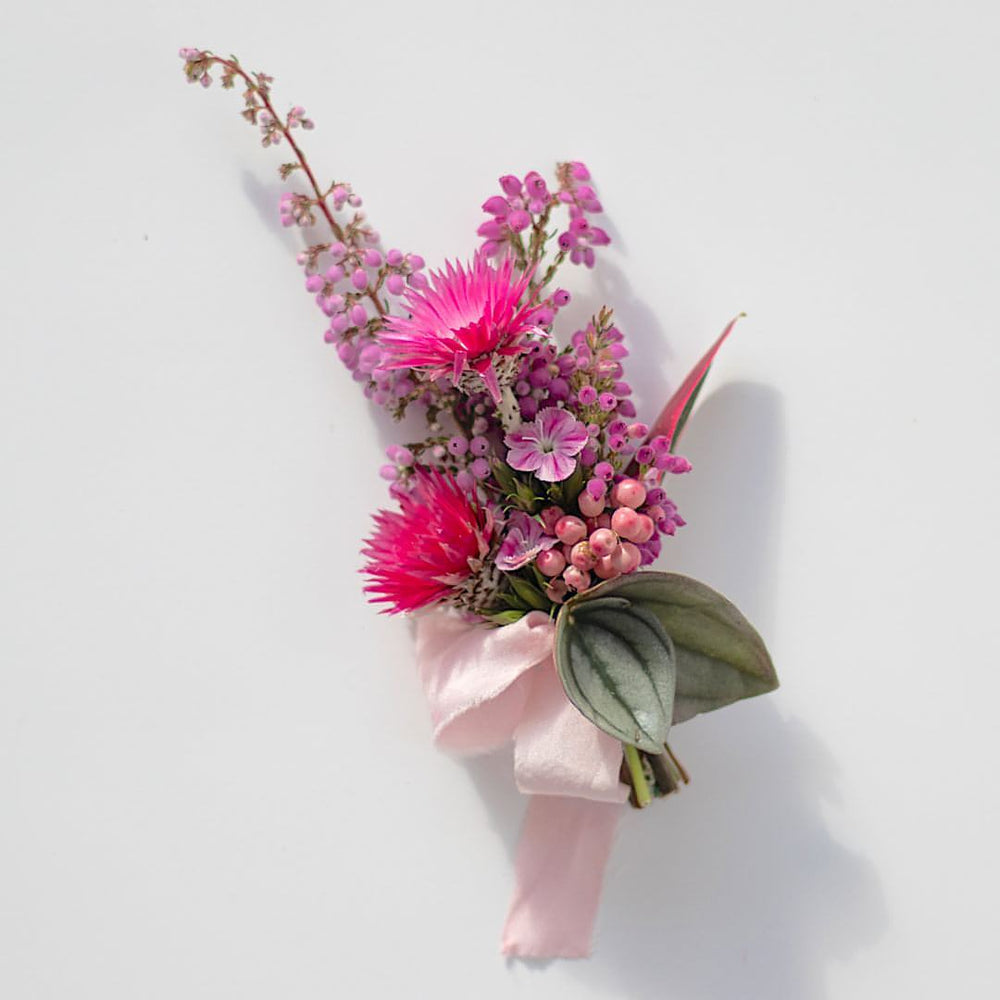 Delicate flowers make up a hot pink boutonniere, which is wrapped in soft pink silk.
