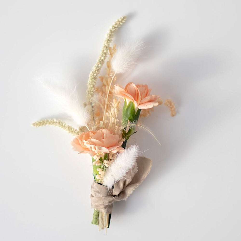 A groom's boutonniere with peach roses and bunny tails, wrapped with a tan satin cloth.