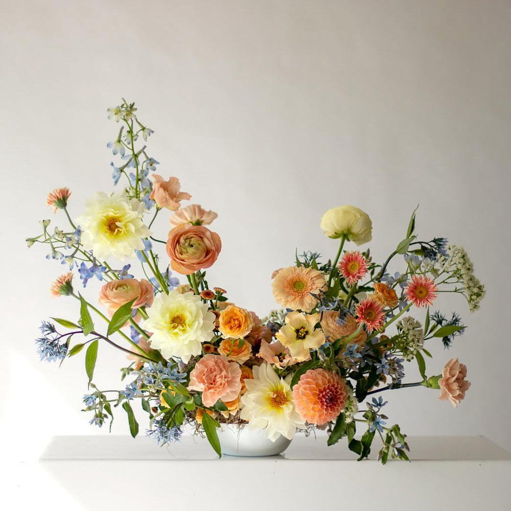Muted orange floral arrangement with cream and light blue accents in a white bowl.