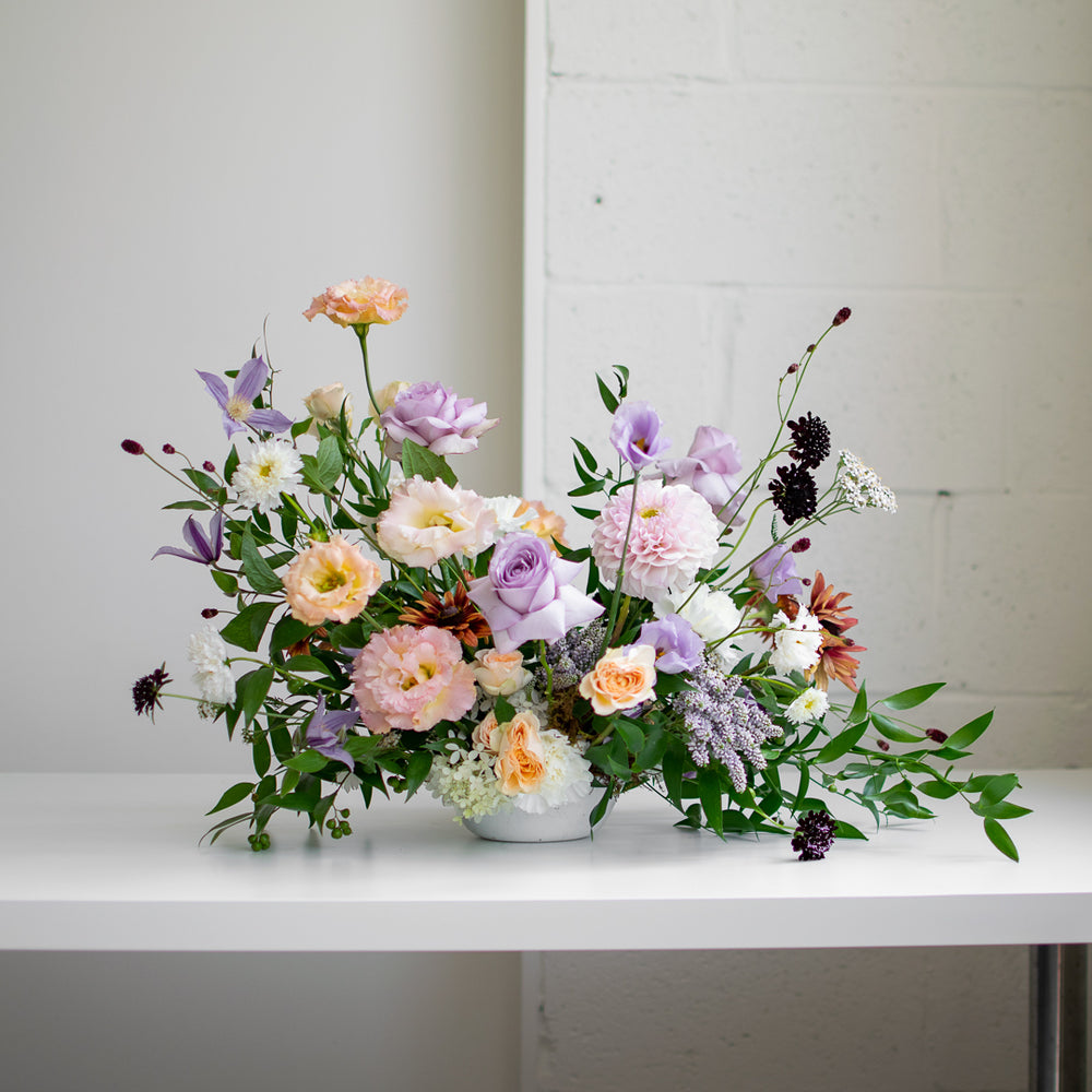 Luscious, soft purple and peachy blooms burst out of vibrant greens in this wedding arrangement.