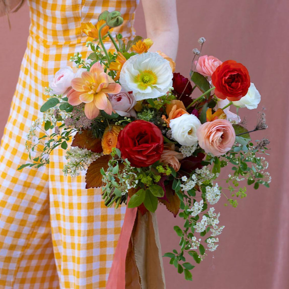 A person wearing yellow gingham overalls holds a bouquet of bright, fresh flowers.