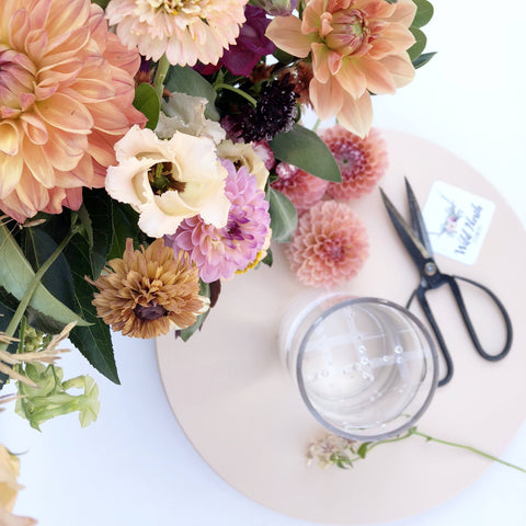 Top-down view of a floral arrangement next to a gridded glass vase and black floral clippers on a lazy susan.