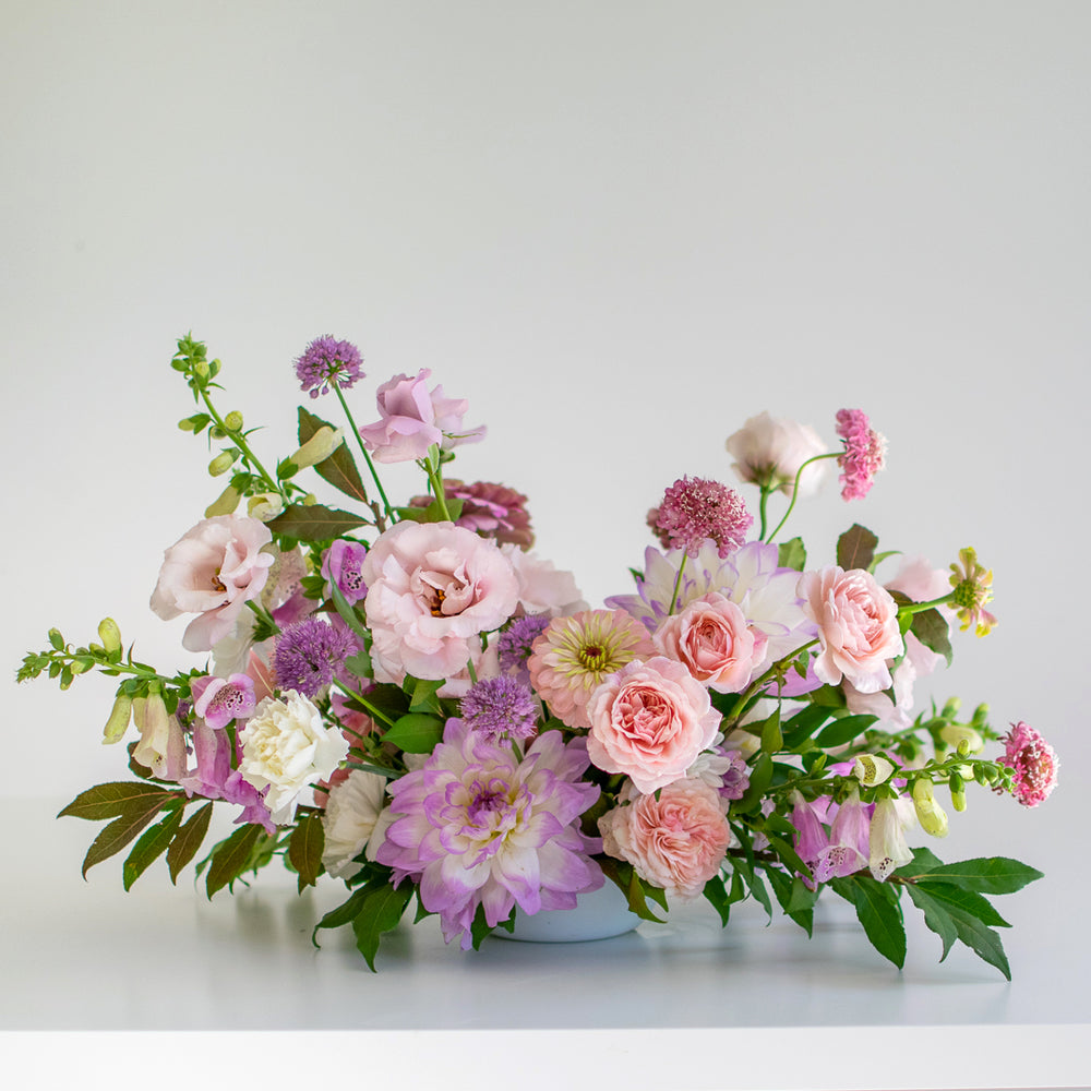 A light pink and purple centrepiece with chrysanthemums and bright greenery.