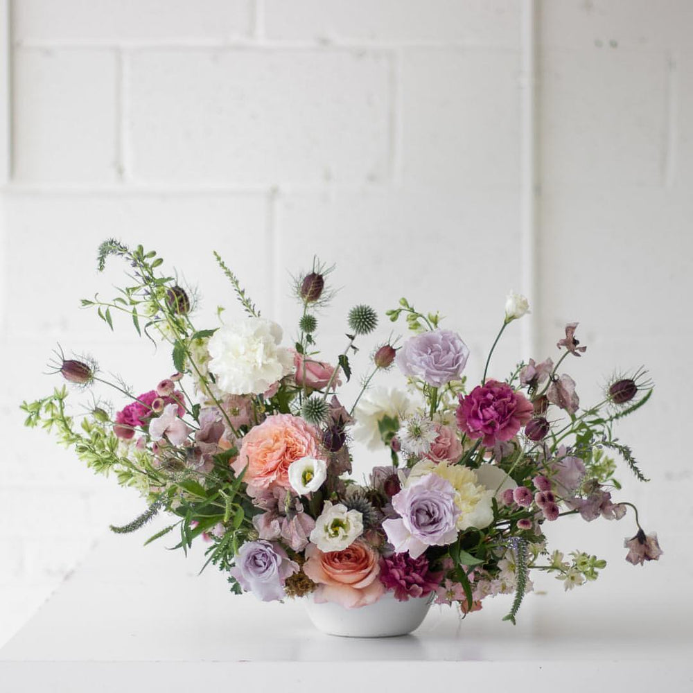 A large, fresh floral arrangement in a whimsical soft pink, purple, and white palette.