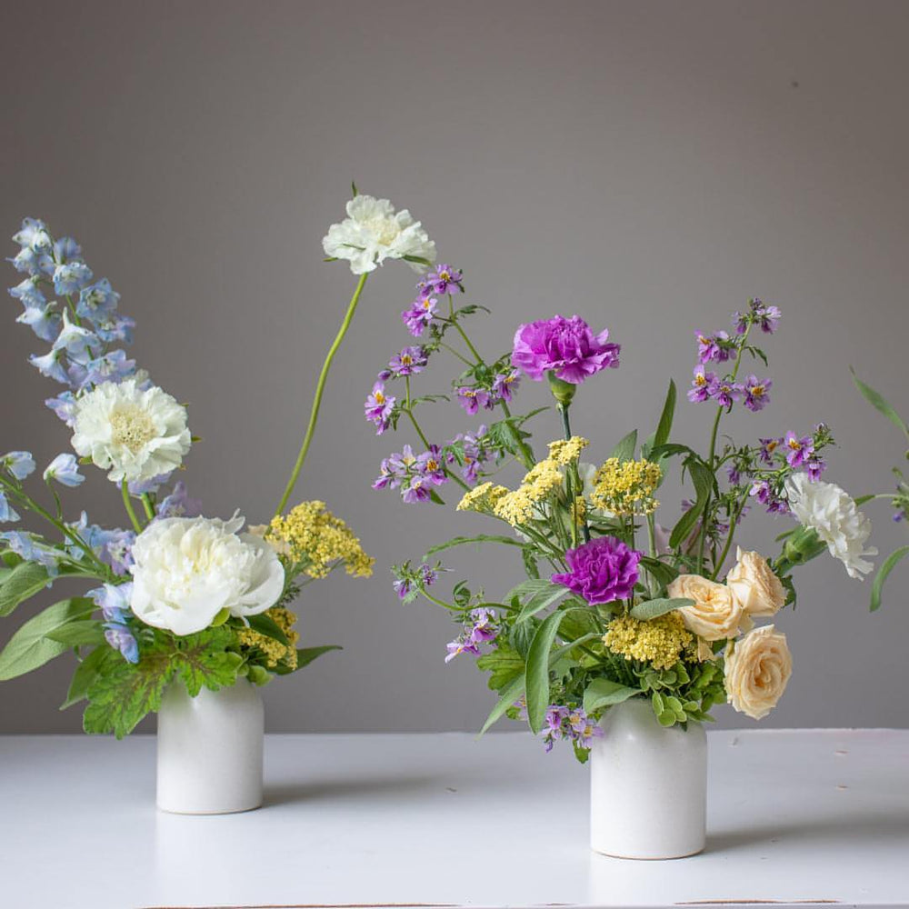 A close of two bud vases with yellow accents. One is blue and white, while the other is primarily purple.