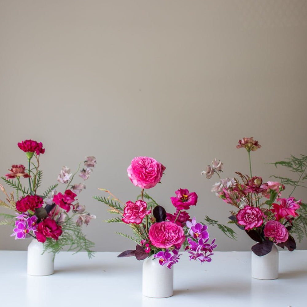 A trio of small floral arrangements in bright pinks and magentas .