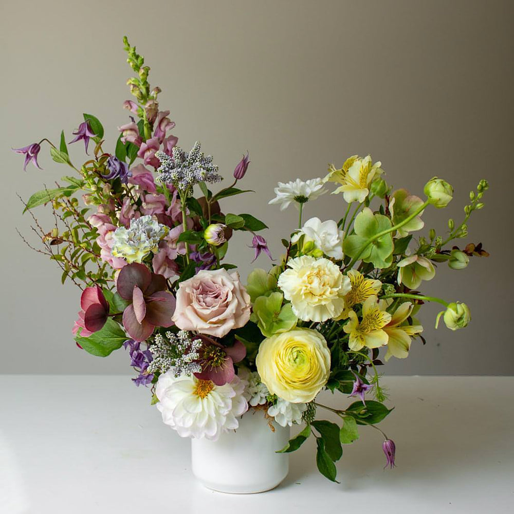 Large purple and white floral arrangement in a soft, muted palette and white ceramic vase
