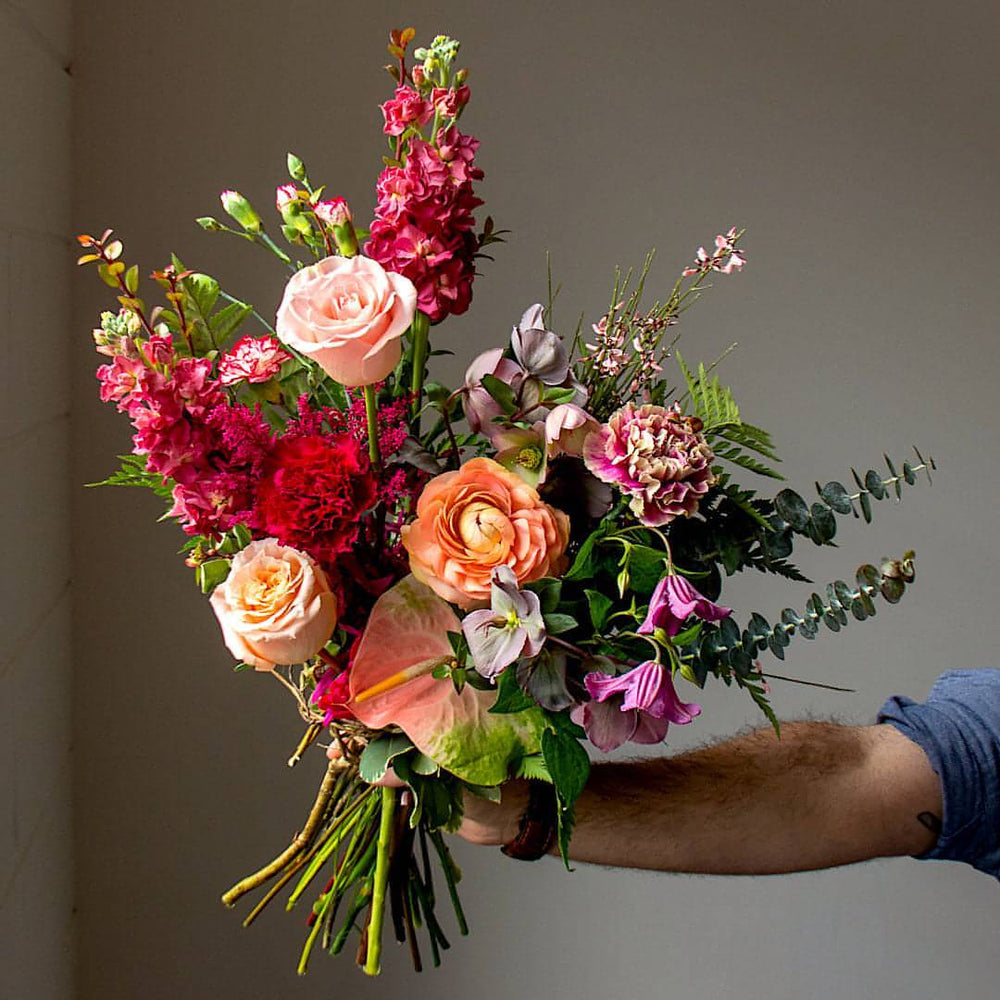 A pink-toned flower arrangement is held out by a man's arm.